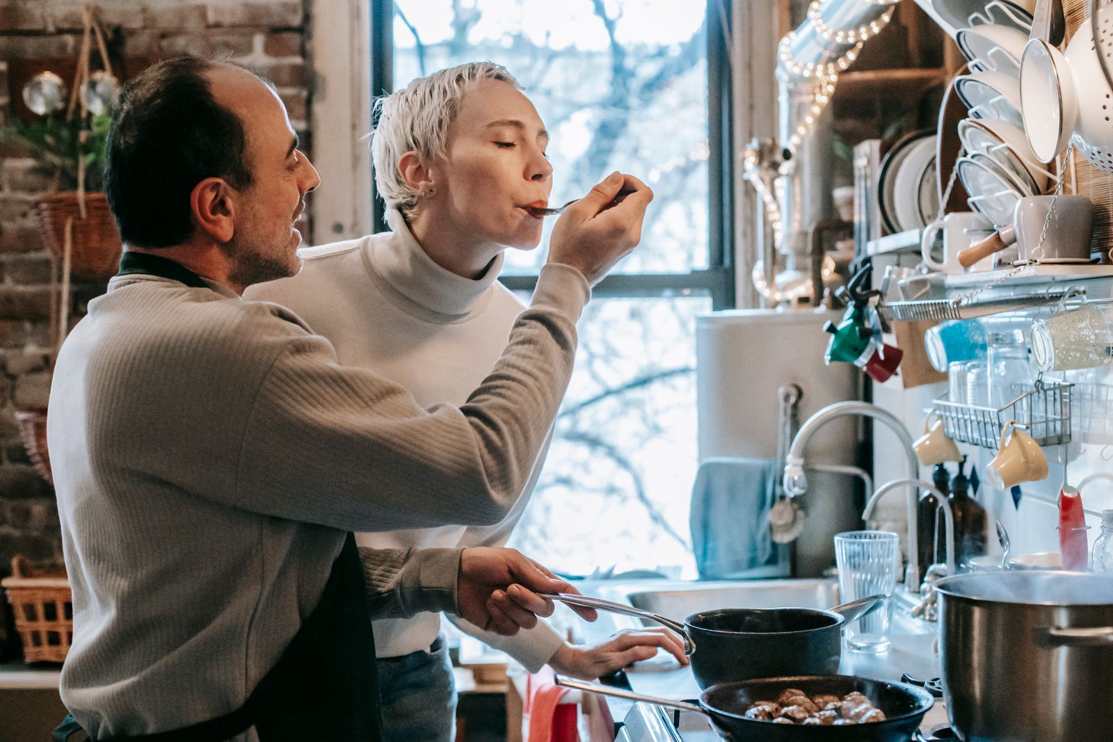 Couple cooking and tasting food together in their kitchen