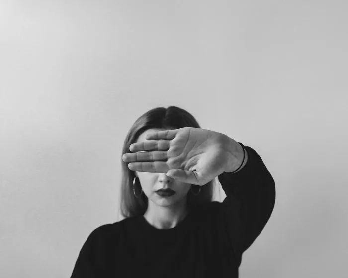 Black and white portrait of a woman covering part of her face with her hand, symbolizing boundaries and self-protection.