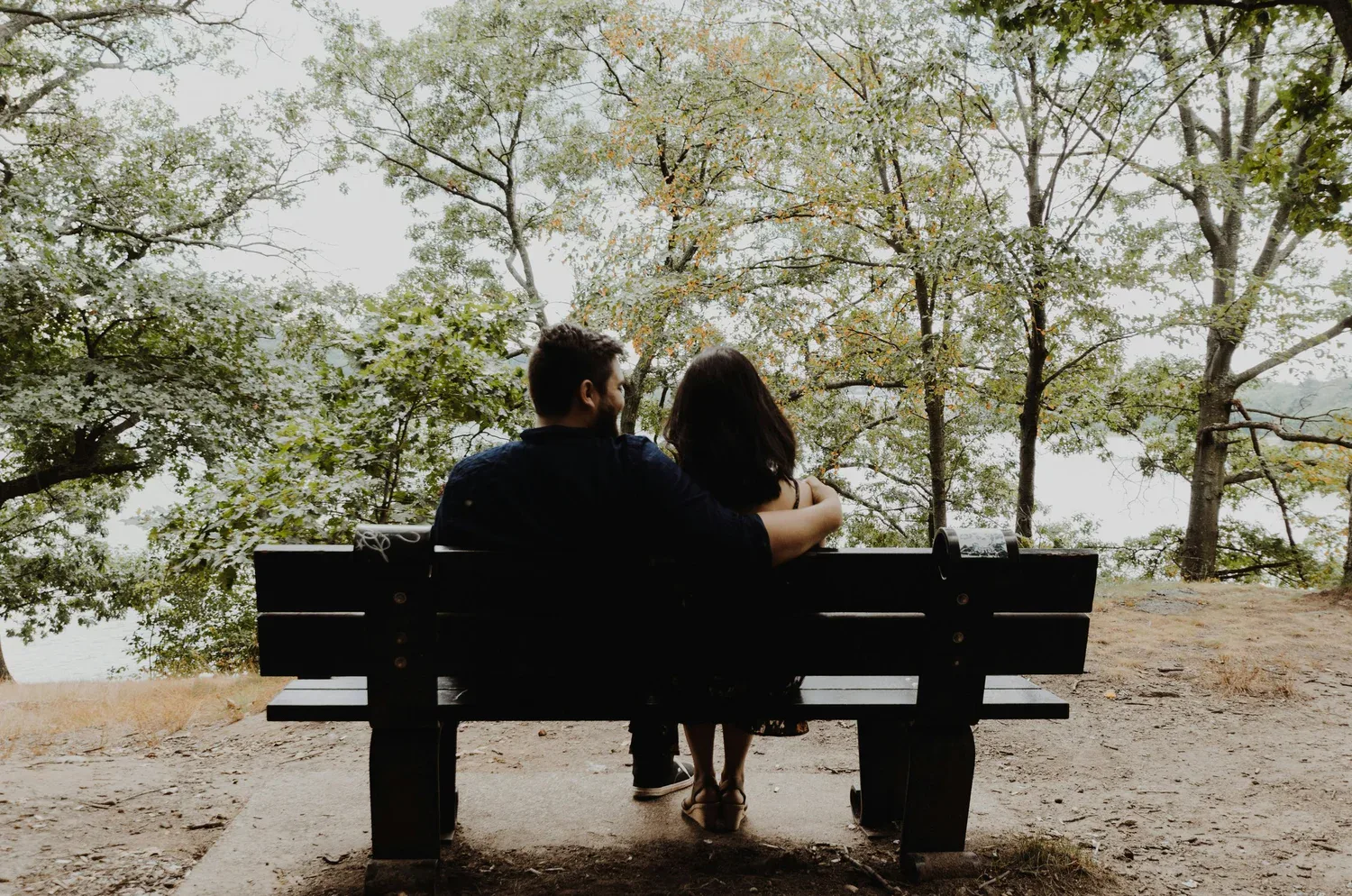 Couple sitting close on a park bench surrounded by trees, representing intimacy, reflection, and renewed commitment in the new year.
