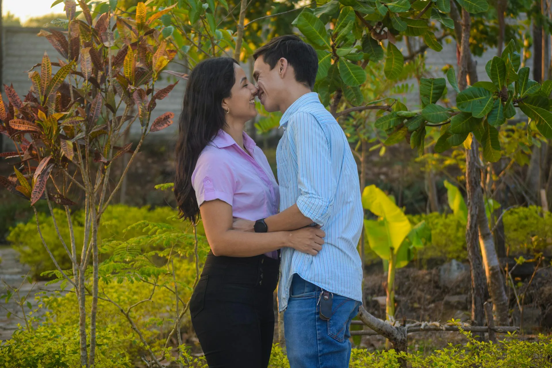 Couple embracing and smiling in a garden surrounded by green plants, showing affectionate intimacy.