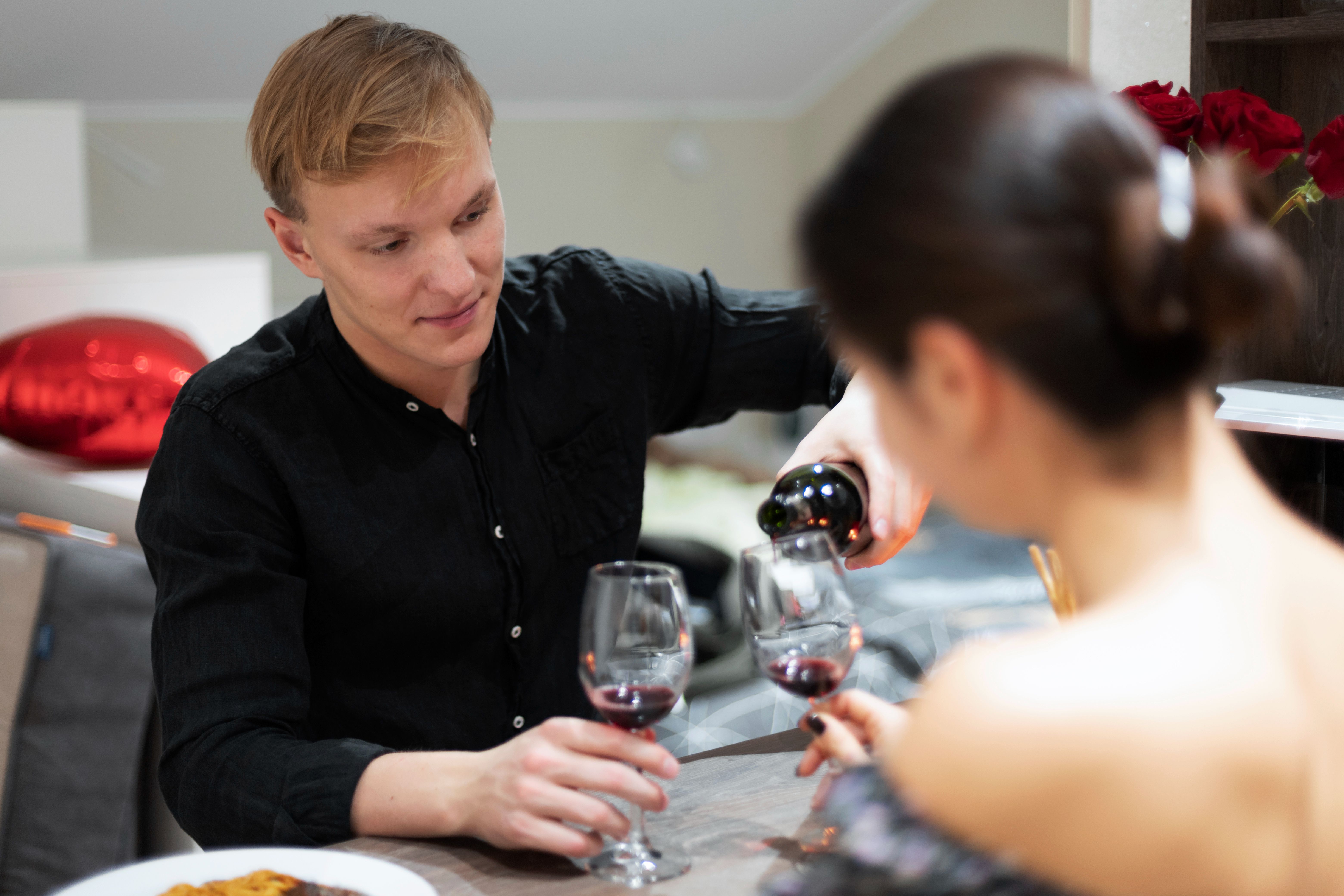 Man pouring red wine during a romantic Valentine's Day dinner with his partner at home.