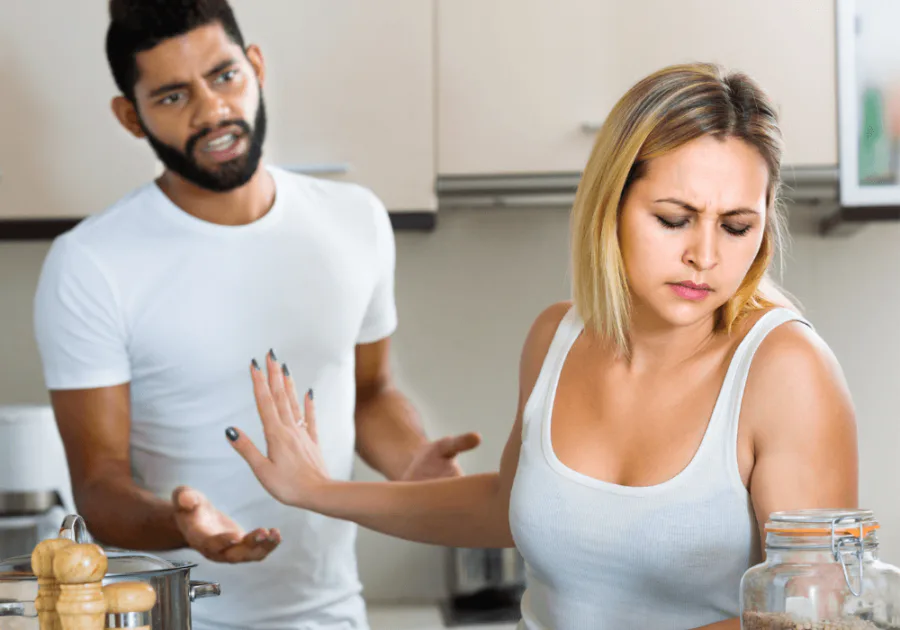 A couple arguing in a kitchen, with a woman holding up her hand to create distance during conflict.