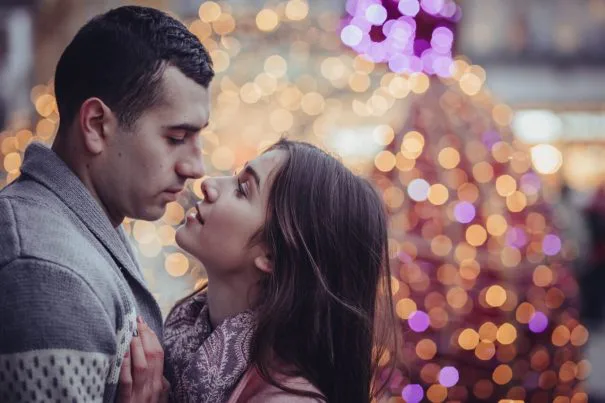 A couple standing close together with festive lights in the background, expressing intimacy, longing, and emotional tension.