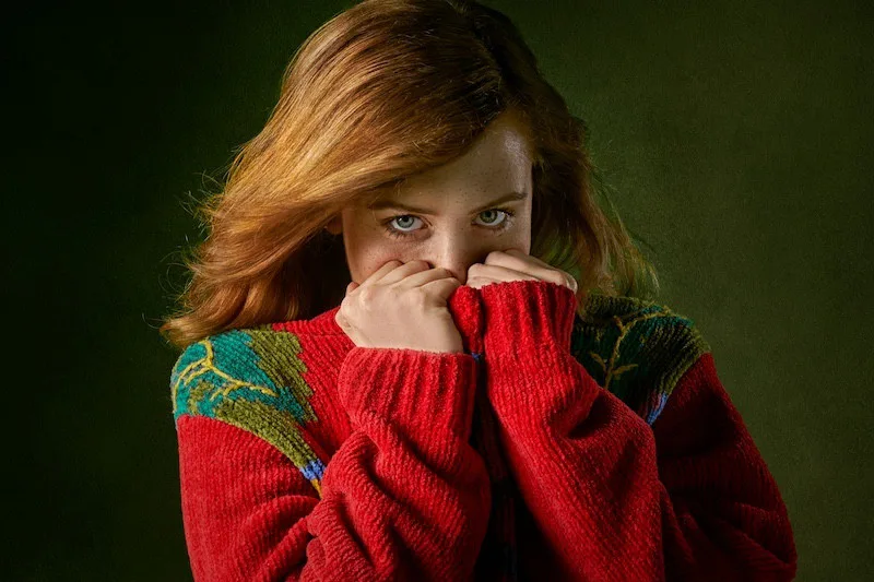 Young woman in a colorful sweater covering part of her face, expressing vulnerability, emotional caution, and the need for safety in relationships.
