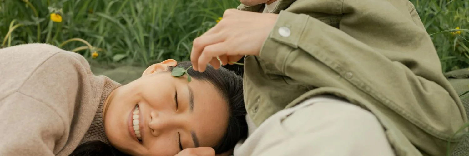 Smiling woman lying on grass beside a partner, conveying emotional safety, comfort, and trust
