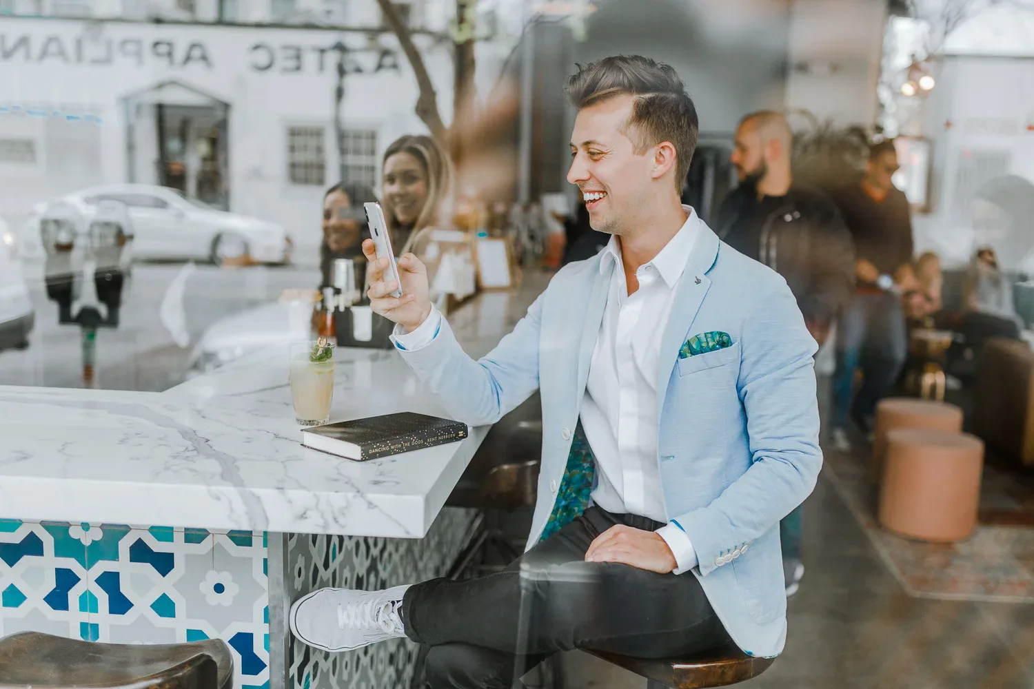 Man sitting in a cafe smiling at his phone, representing digital communication and sending a New Year love message.