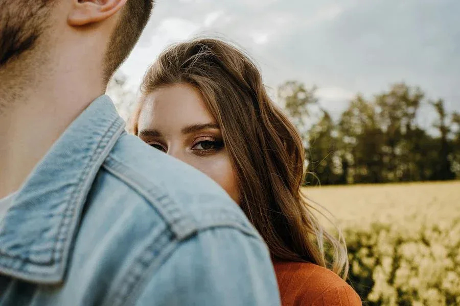 Young woman looking past a man's shoulder in a field, representing emotional attachment, uncertainty, and relationship reflection.