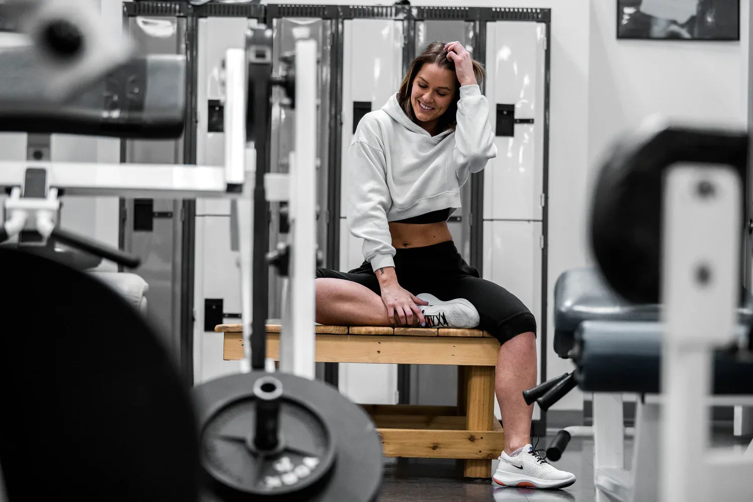 Woman sitting on a bench in a gym, smiling softly in athletic wear among workout machines.