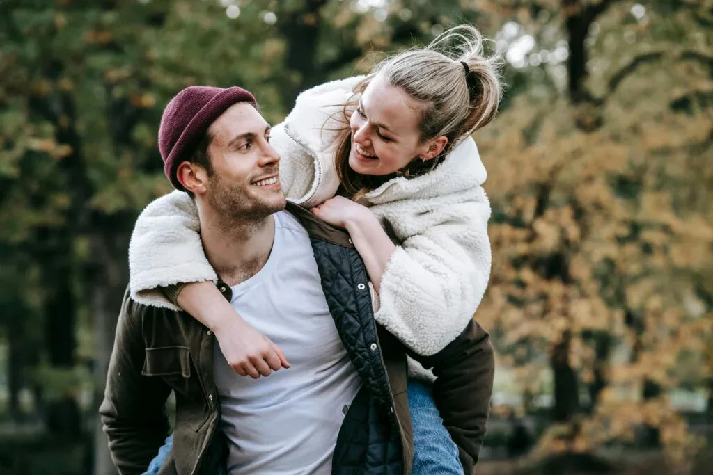 Young couple outdoors smiling and laughing, with one partner on the other's back, symbolizing joy, reconnection, and hope for the new year.