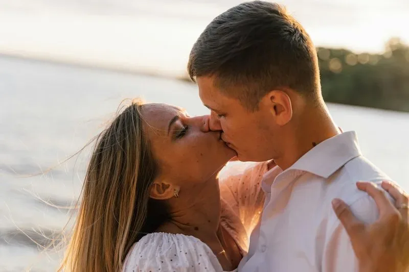 Couple kissing outdoors at sunset in a warm, romantic moment.