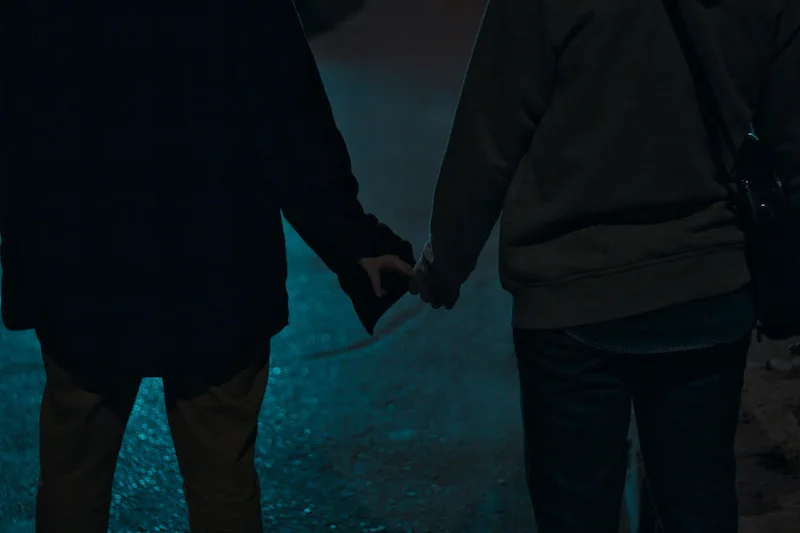 Two people holding hands at night on a dimly lit street, expressing intimacy, safety, and commitment during life transitions.