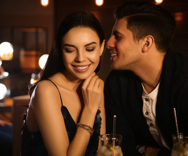 Intimate couple leaning close together in a dimly lit bar sharing a tender private moment