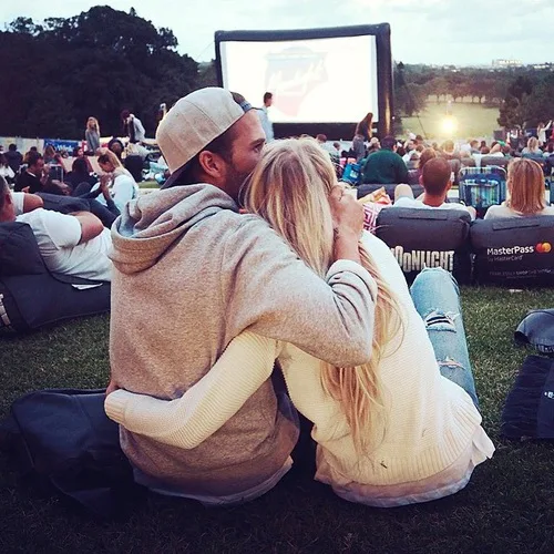 Couple sitting close together at an outdoor movie, embracing on the grass and expressing warmth, comfort, and relationship intimacy.