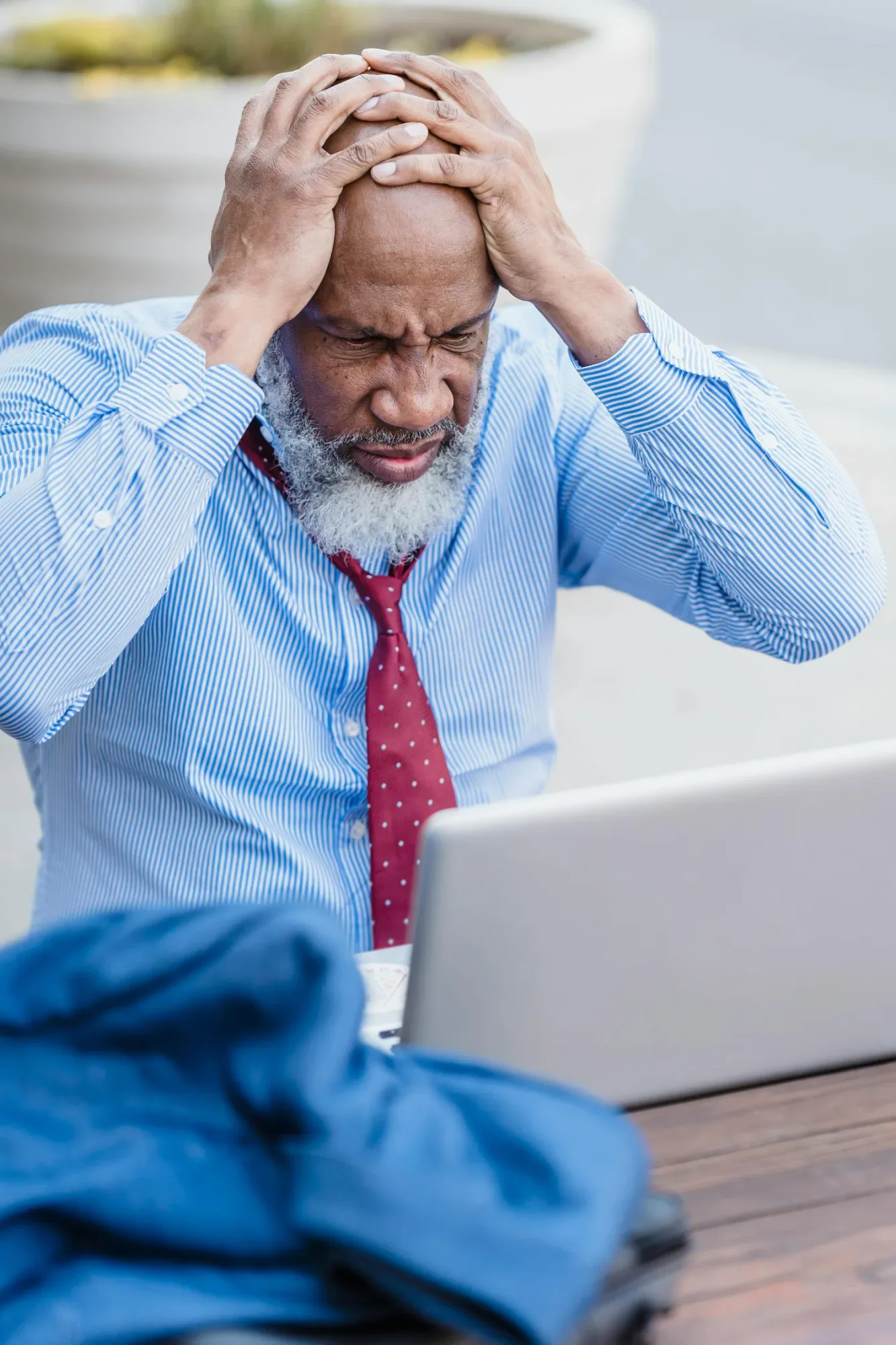 A stressed man holding his head while sitting at a laptop, representing work anxiety and emotional pressure affecting relationships.