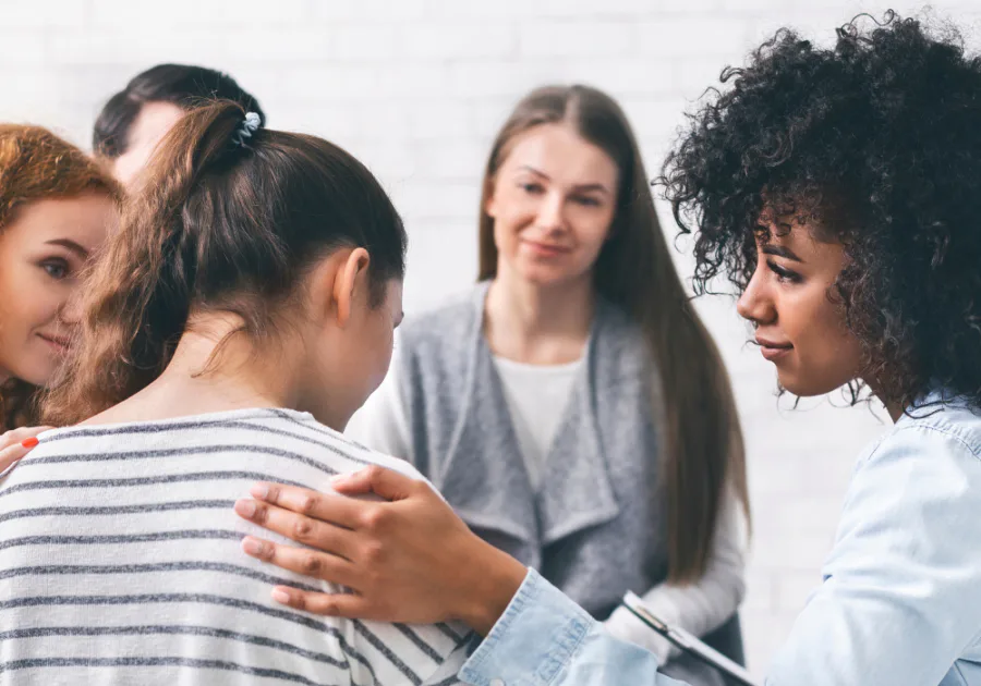 Un pequeño grupo de apoyo consolando a una persona, representando apoyo emocional, vulnerabilidad y confidencias seguras.