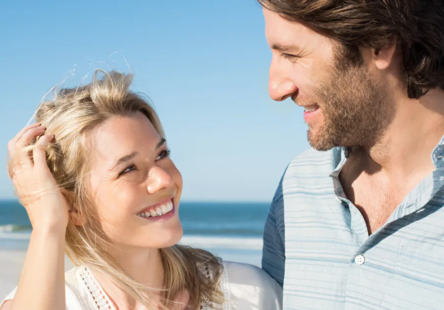 Couple souriant se regardant dans les yeux sur une plage avec l’océan en arrière-plan