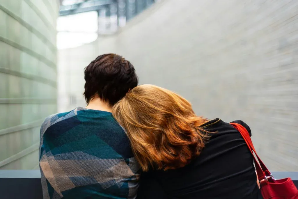 A couple sitting closely on a bench, with one partner resting their head on the other's shoulder, conveying comfort, support, and emotional intimacy.