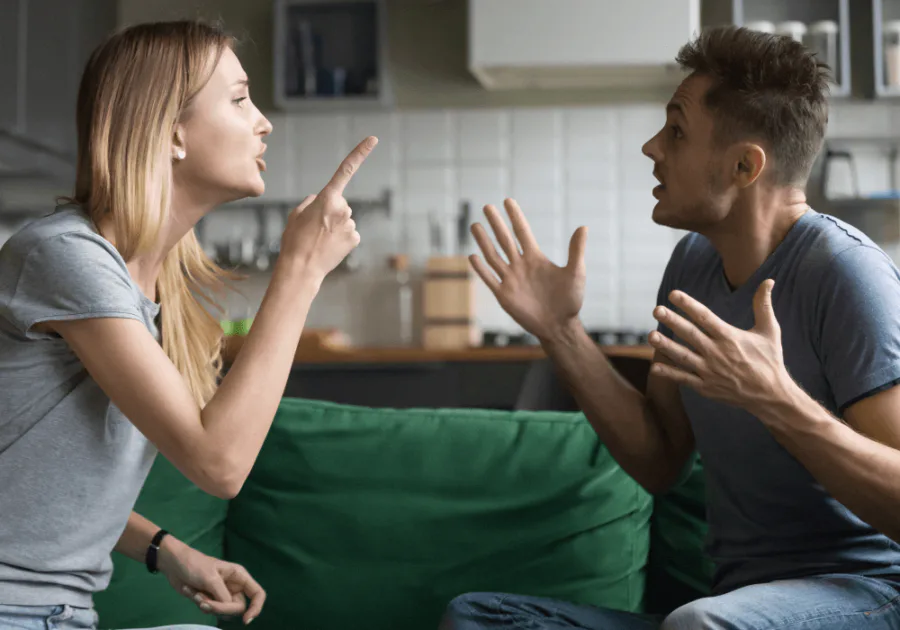 A couple arguing in a living room, facing each other with intense gestures, representing relationship conflict and emotional escalation.