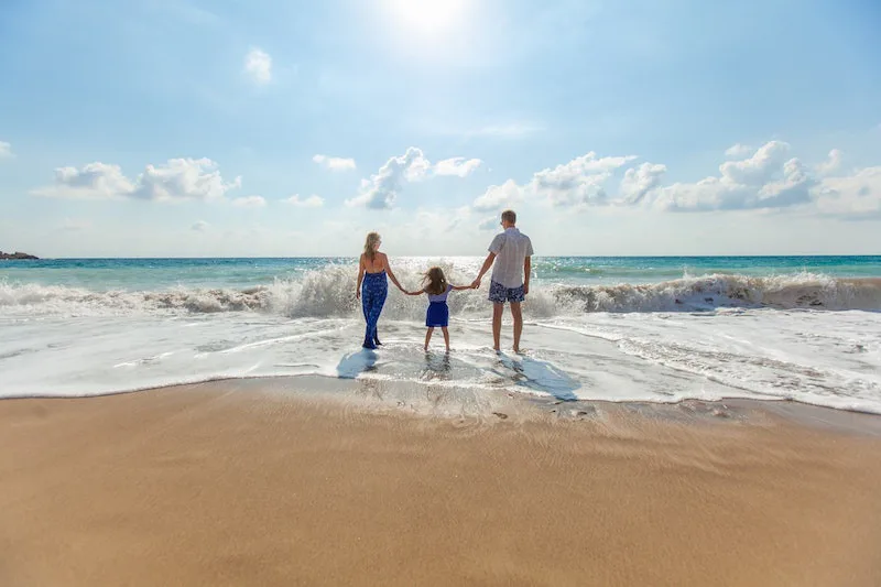 Parents and child holding hands at the ocean, representing emotional security, family connection, and marriage hopes.