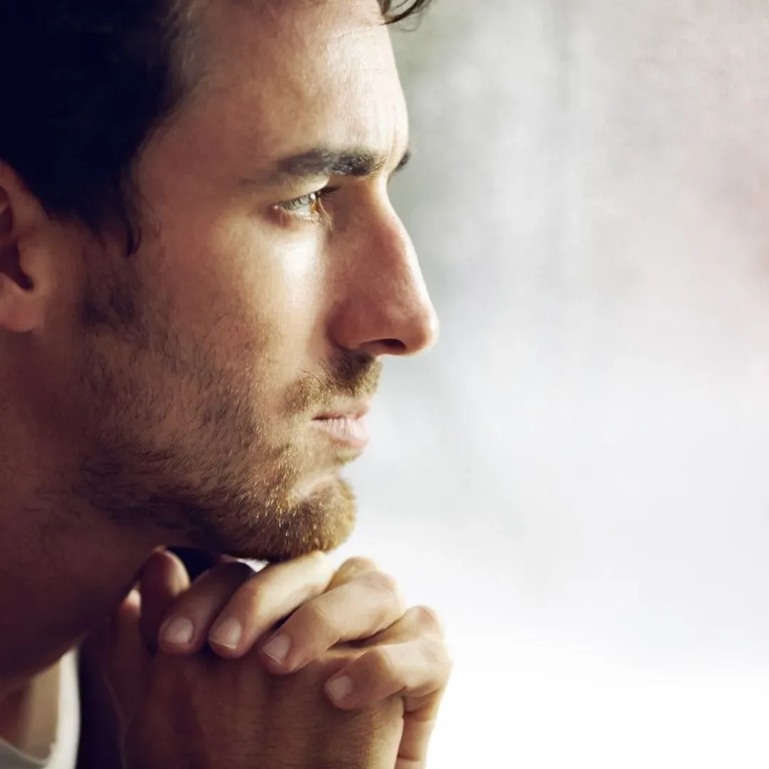 Thoughtful man in side profile with hands near his chin, conveying introspection, emotional stress, and relationship reflection.