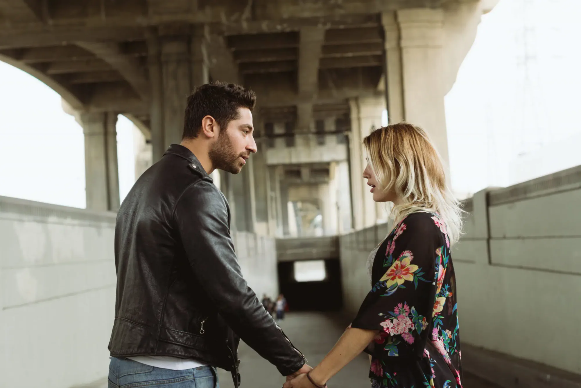 A couple holding hands under an overpass during a serious conversation, symbolizing relationship conflict, uncertainty, and possible reconciliation.