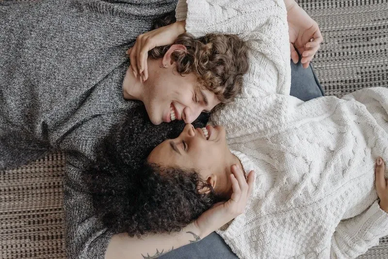 A happy couple lying close together and smiling, representing tenderness, intimacy, and emotional safety in a loving relationship.