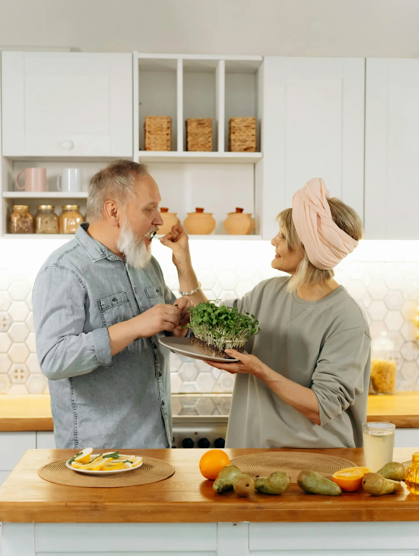 Mature couple sharing a tender moment in a kitchen, feeding each other and smiling, symbolizing everyday love, care, and emotional support.