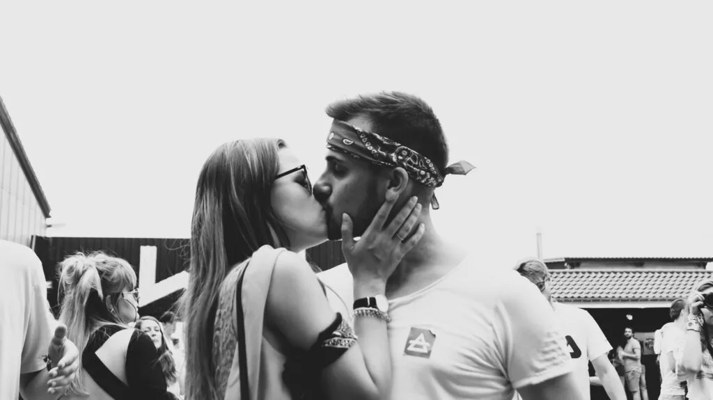 Couple kissing at an outdoor gathering, expressing romantic chemistry, affection, and celebratory wedding energy.