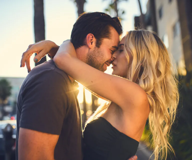 Una pareja abrazándose al aire libre al atardecer, simbolizando afecto público consensuado y conexión romántica.