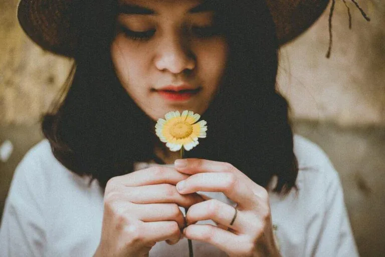 Young woman holding a flower in a reflective moment, symbolizing softness, self-love, and emotional renewal in the new year.