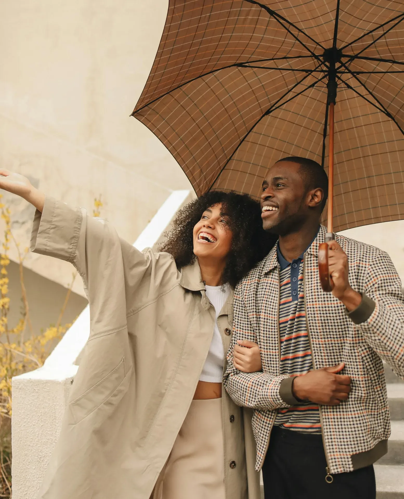 Happy couple standing under an umbrella outdoors, smiling and looking ahead, representing encouragement and celebration after graduation.