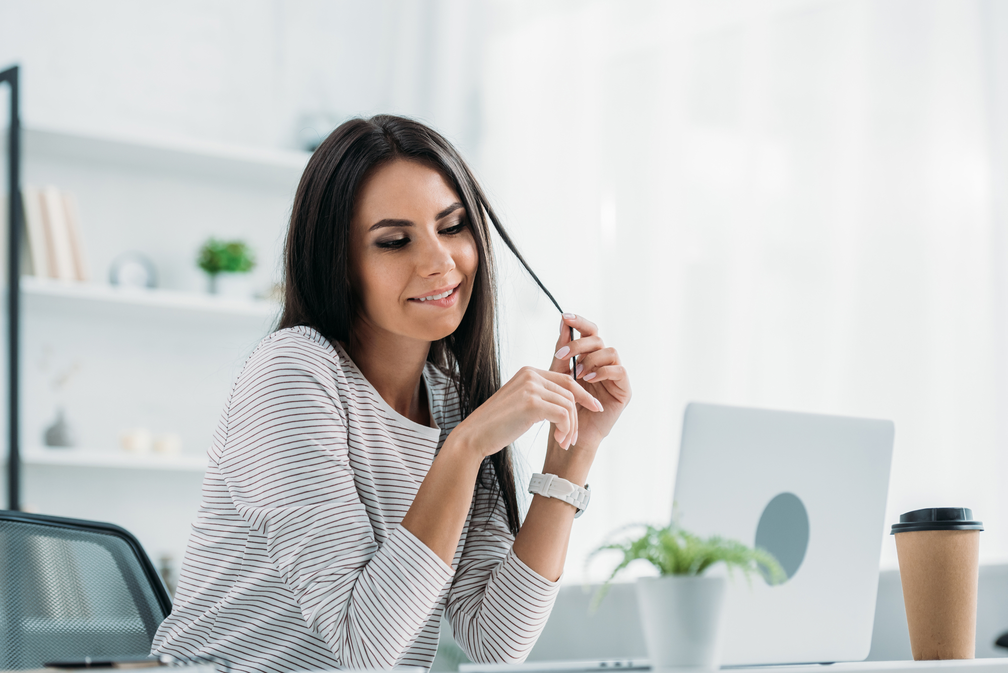 Woman smiling thoughtfully at a laptop in a bright room, writing a meaningful digital letter for her mom.