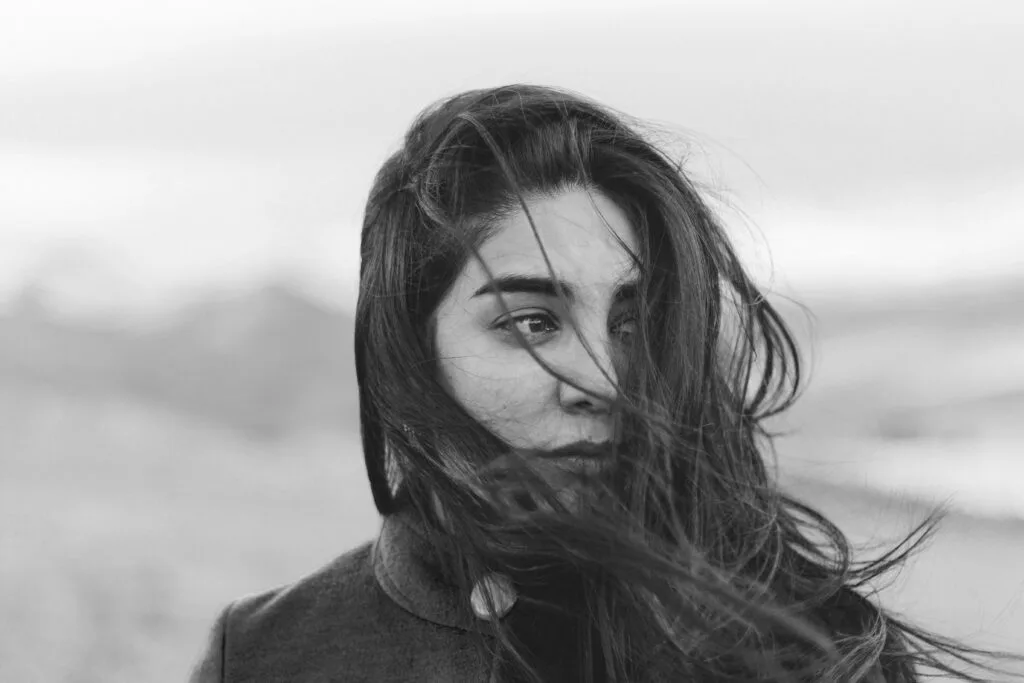 Black and white portrait of a woman outdoors with windblown hair, expressing introspection, heartbreak, and emotional transition.