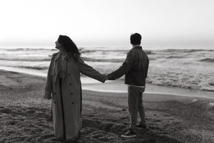 Couple holding hands on a beach in black and white, representing commitment, partnership, and a lifelong journey together.