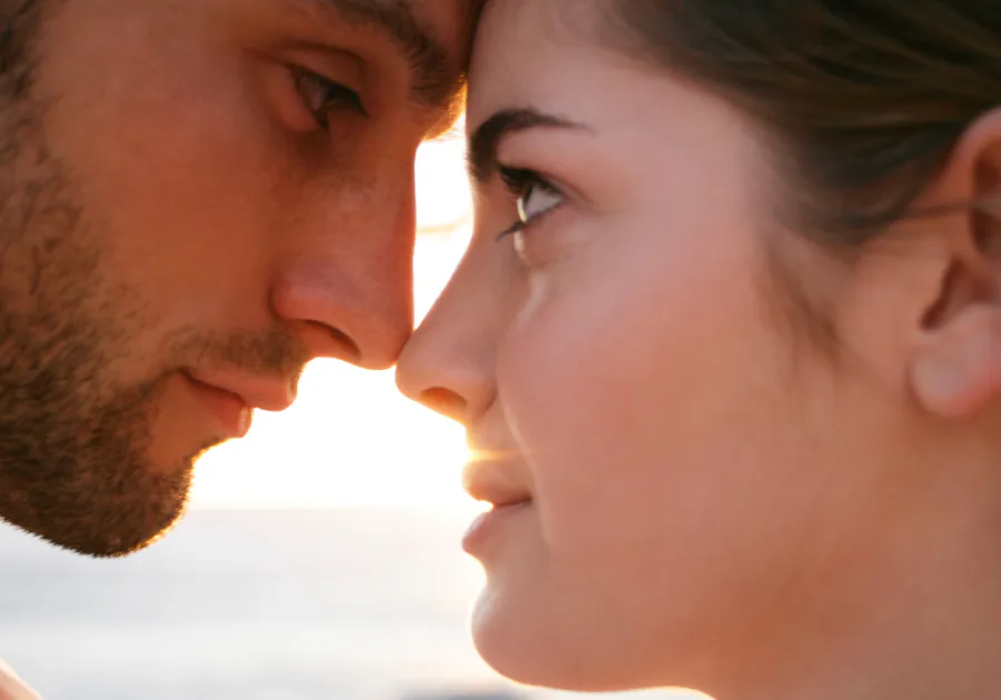 Gambar dekat sepasang kekasih saling memandang ke mata ketika matahari terbenam, menyampaikan debaran romantik dan komitmen yang semakin mendalam.