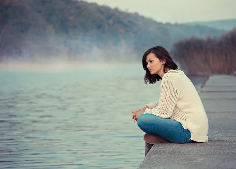 Thoughtful woman sitting by a lakeside, conveying introspection, solitude, and emotional reflection before commitment.