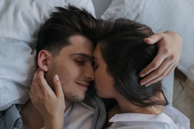 Couple lying close together in bed, embracing softly and showing emotional intimacy and romantic closeness.