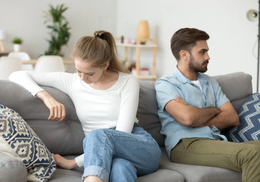Couple sitting apart on a couch looking emotionally disconnected and distant from each other