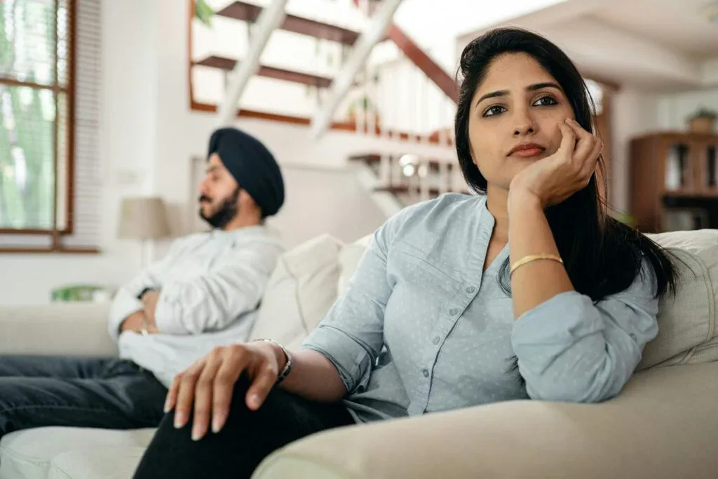 Married couple sitting apart on a couch, showing emotional distance and challenges with intimacy in marriage.