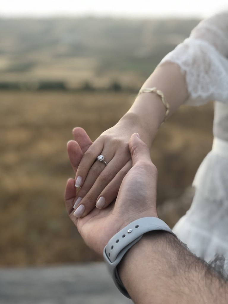 Close-up of a man holding a woman's hand with an engagement ring.