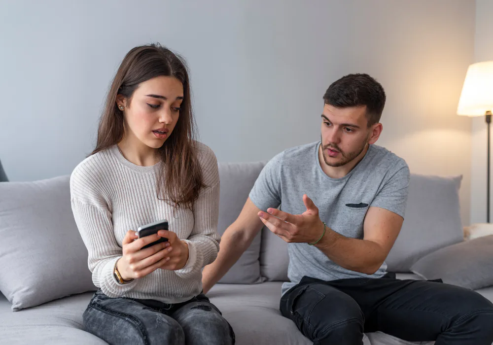 Couple sitting on a couch during a tense conversation while the woman looks at her phone.