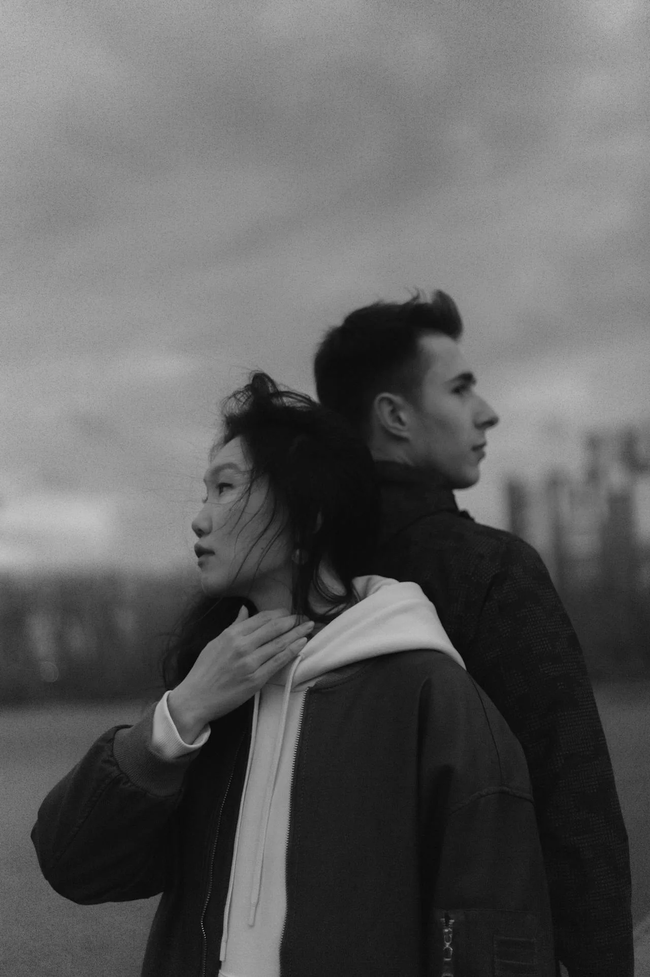Black and white portrait of a couple standing back to back, looking away with emotional distance