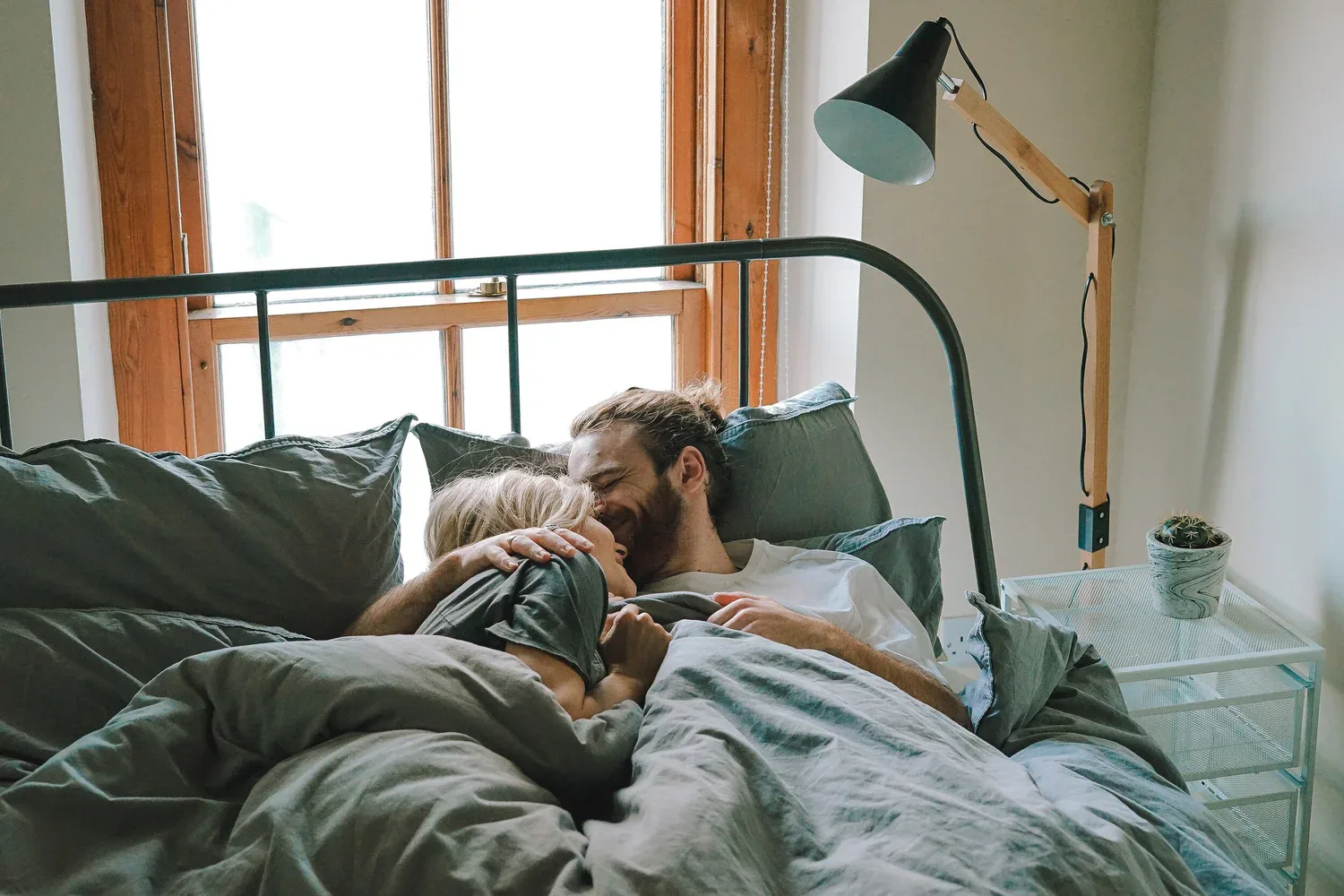 Couple cuddling in bed near a window, representing emotional safety, warmth, and married intimacy