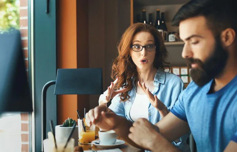 Woman speaking emphatically to a withdrawn partner at a table, representing communication problems in relationships during the holidays.