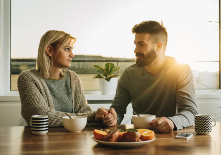 Casal sentado à mesa de mãos dadas durante uma conversa séria, simbolizando reparação emocional, compromisso e cura no relacionamento.