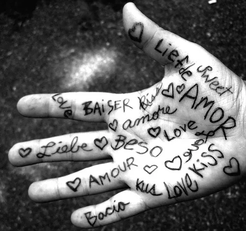 Black and white photo of a hand with love words written in multiple languages and small heart drawings.