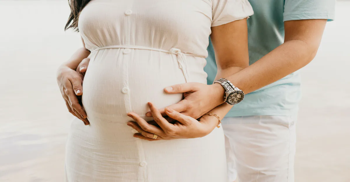 屋外で、妊婦のお腹をパートナーふたりの手がやさしく包むクローズアップ。